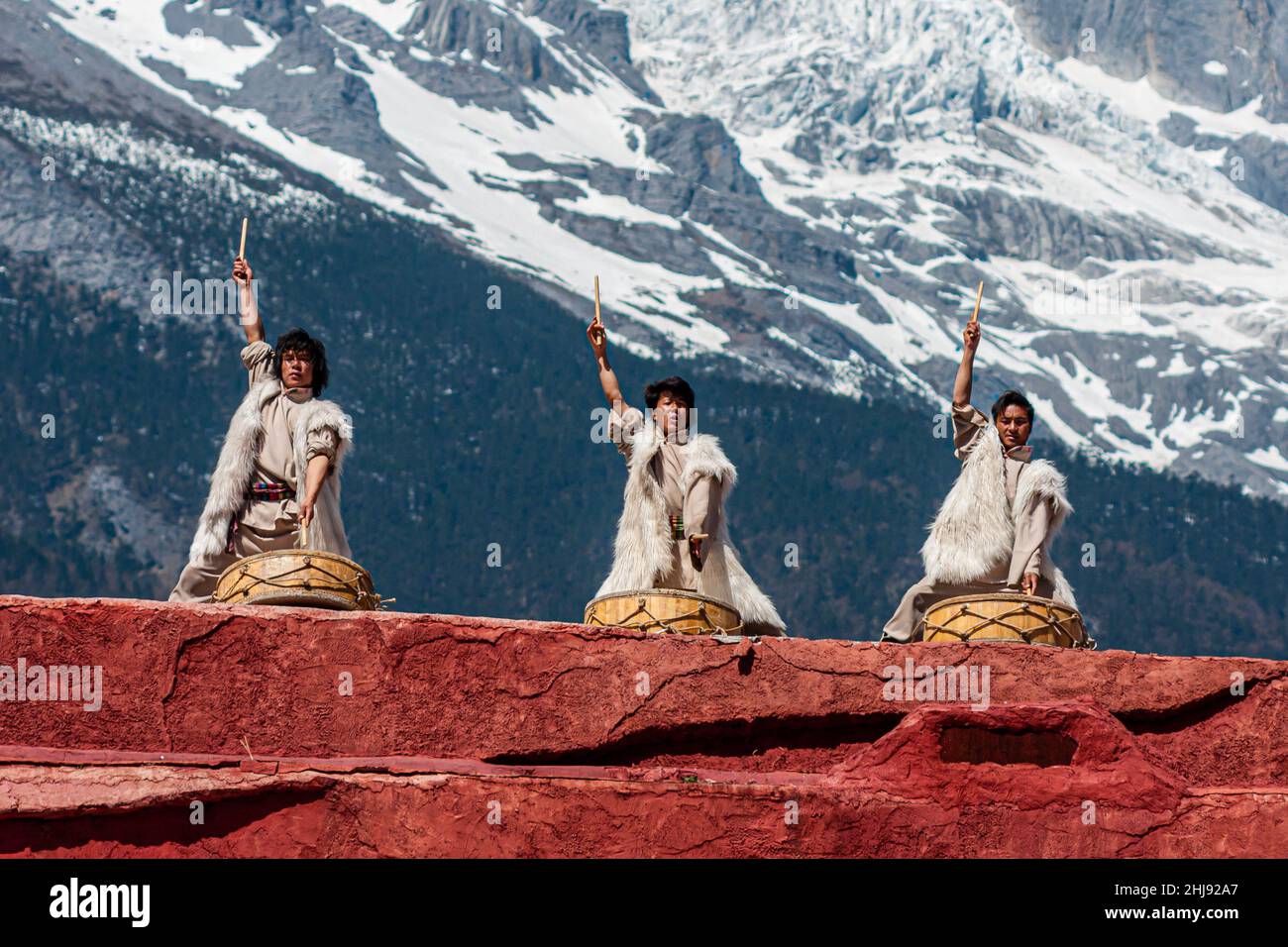 The ethnic minority of the Naxi people in their traditional costumes; scene from a performance with the Jade Dragon Snow Mountain in the background Stock Photo