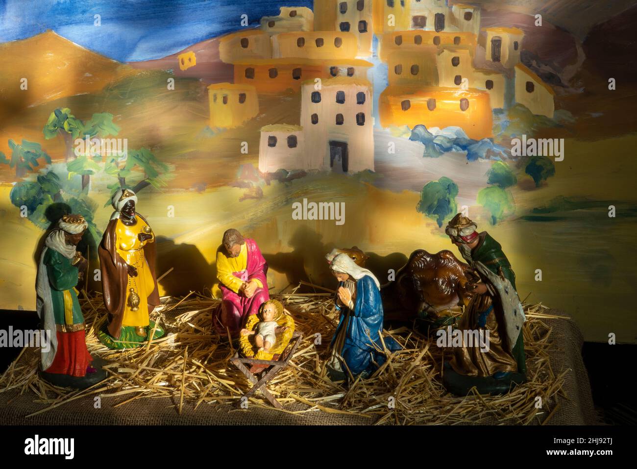 A nativity scene created with model figures on straw against a pained backdrop of ancient houses, at  All Saints Church, Easton, Suffolk Stock Photo