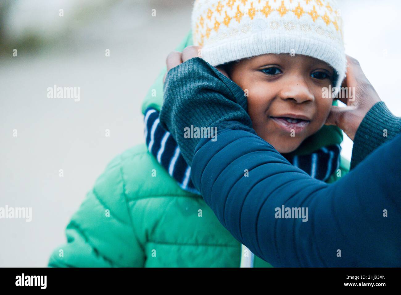 A cheerful African American preschooler boy in winter clothes and hands fixing his hat Stock Photo