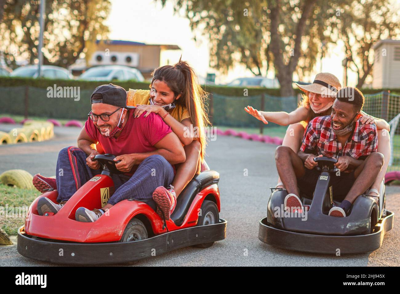 Group of multiracial friends having fun with go kart  - Young people with face mask on smiling and cheerful at mini car racing - Couples outside in do Stock Photo