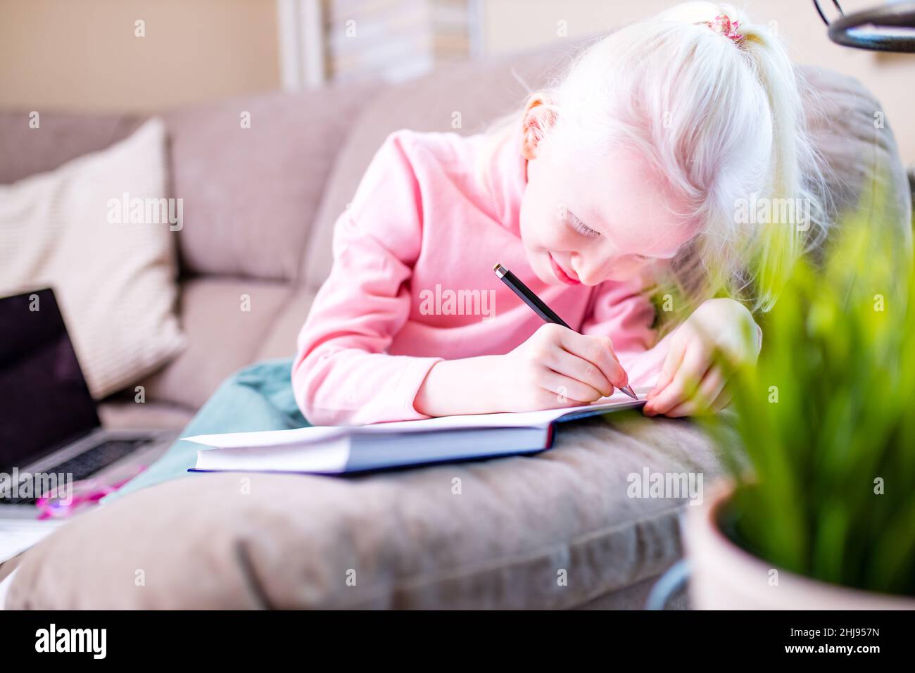 beautiful little girl getting online distance lesson in living room Stock Photo