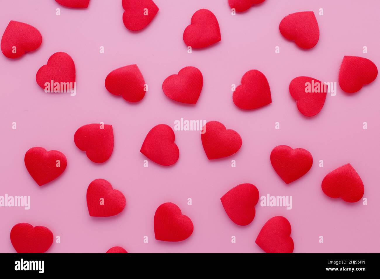 Lots of small, red fabric hearts, placed on a soft pink background in honor of the holiday of love and lovers. Romantic wallpaper. Stock Photo