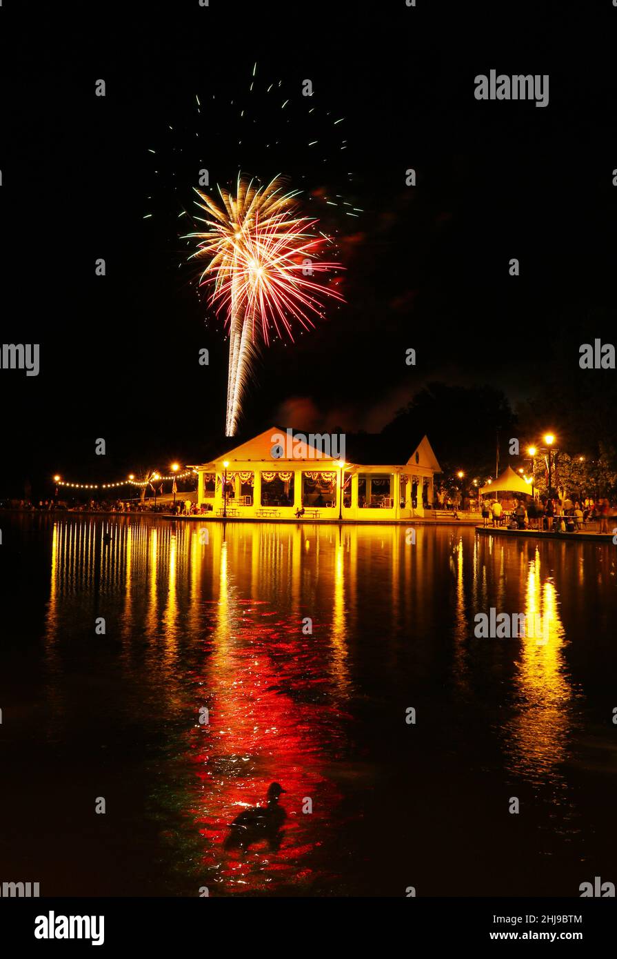Fireworks over Shawnee Park pavilion. July 4th, Independence Day, celebration. A duck swims in the foreground. Shawnee Park, Xenia, Dayton, Ohio, USA. Stock Photo
