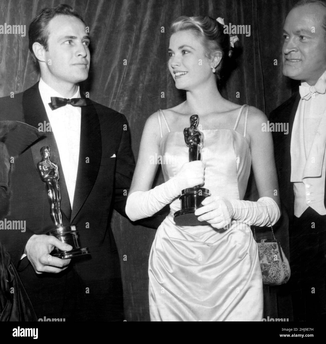 March 30, 1955, New York, New York, USA: MARLON BRANDO (L) and GRACE KELLY holding their oscar statuettes at the 27th Academy Awards, with host BOB HOPE at right. Kelly won Best Actress for her performance in 'The Country Girl'. Marlon Brando was Best actor winner for his performance in the movie 'On The Waterfront.' (Credit Image: © Globe Photos/ZUMA Wire) Stock Photo