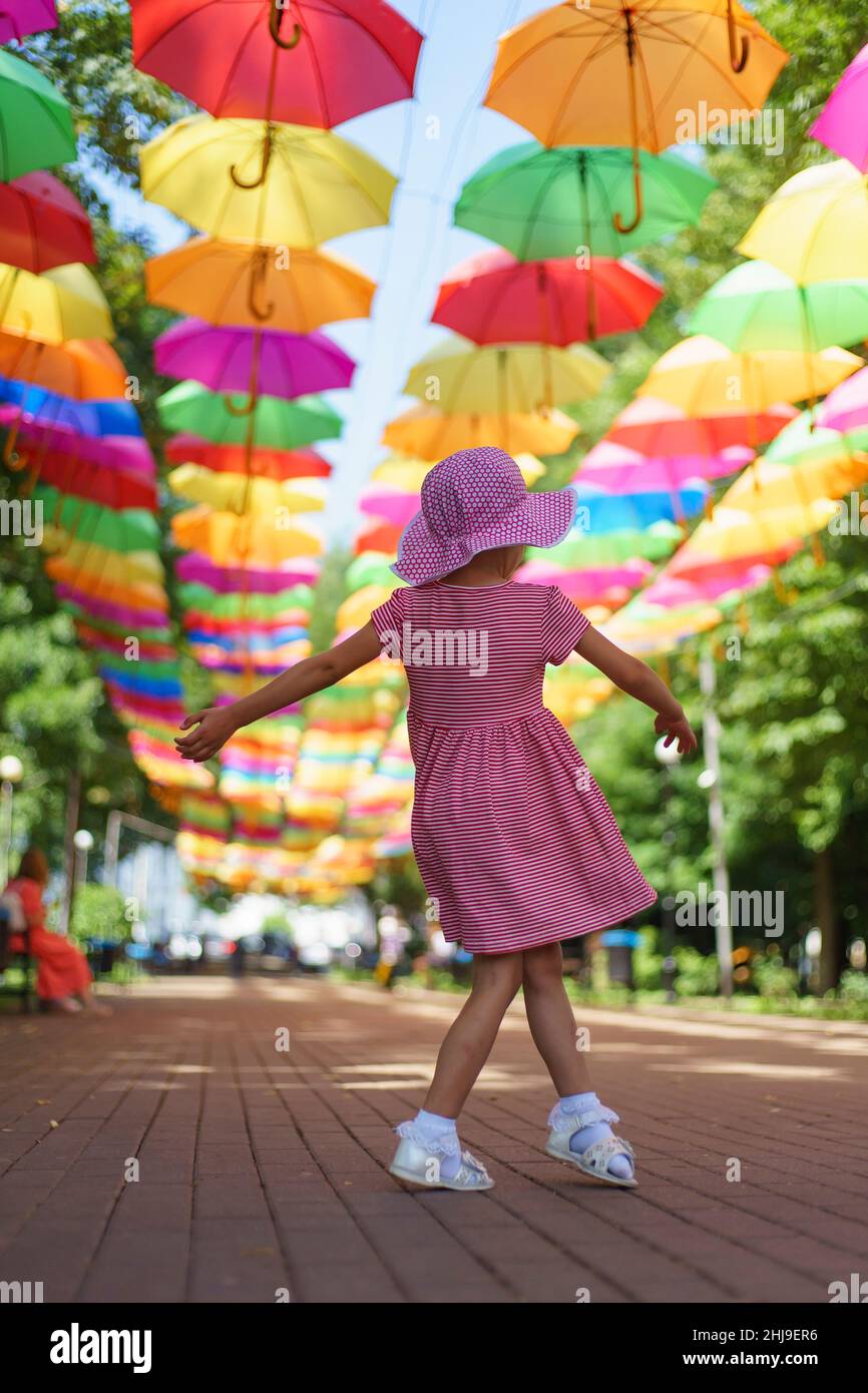 girl in pink dress spinning under many colored umbrellas , umbrella