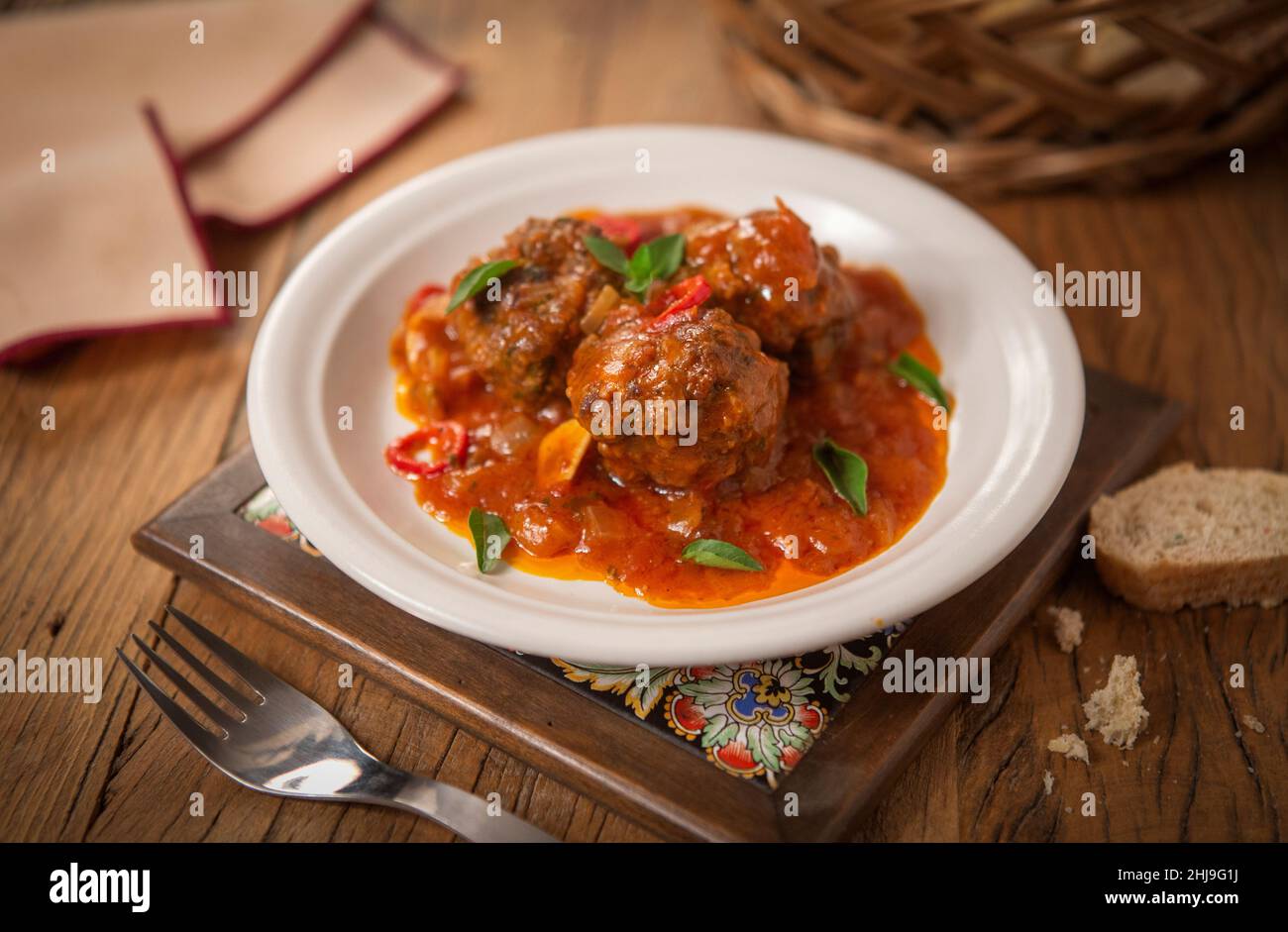 Deliciosas almôndegas de carne bovina ao molho de tomate picante com folhas de manjericão. Em fundo de mesa rústica. Stock Photo