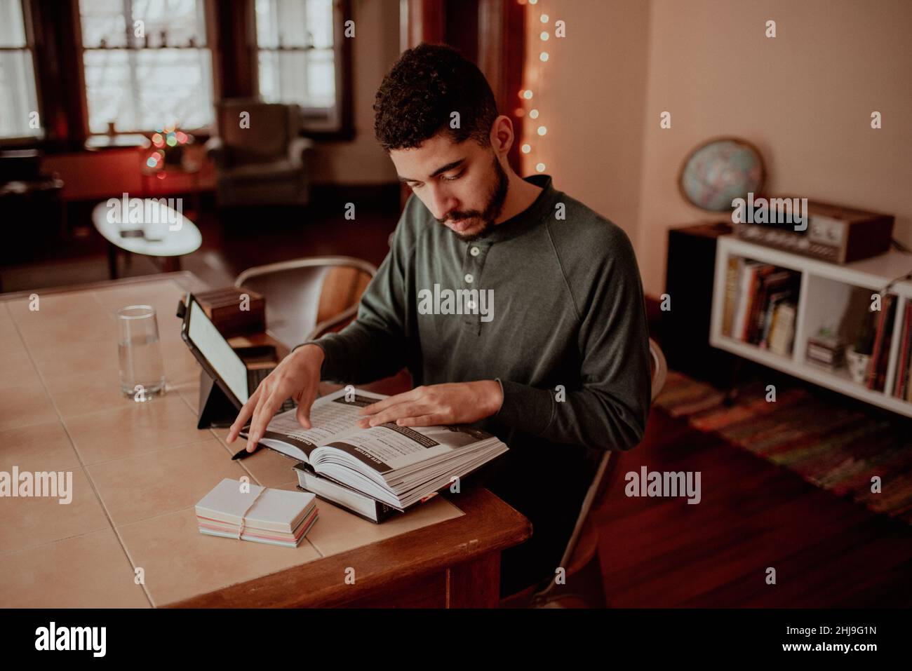 Mixed-race millenial fit man in green long sleeve preps to game master a tabletop fantasy roleplaying game with friends, studying game manual to prep Stock Photo
