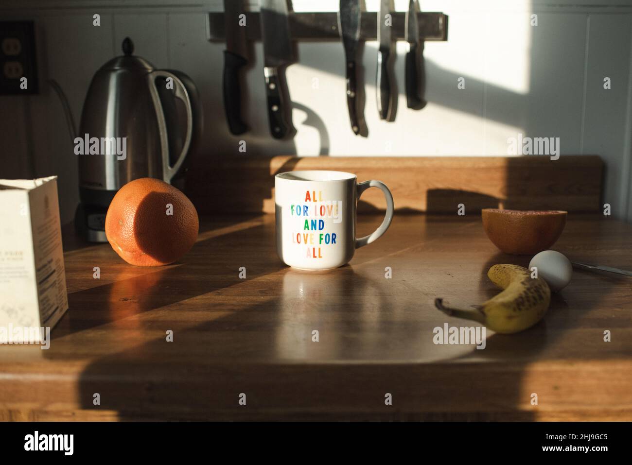 Cute All for Love and Love for All LGBTQ+ mug, rainbow mug, millenial hipster decor, countertop with breakfast foods in the morning light Stock Photo