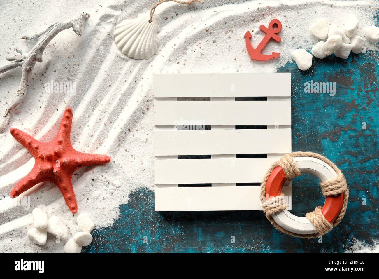 Sand and sea background. White sand on turquoise blue with pebbles, red starfish, anchor, safe ring. Stock Photo