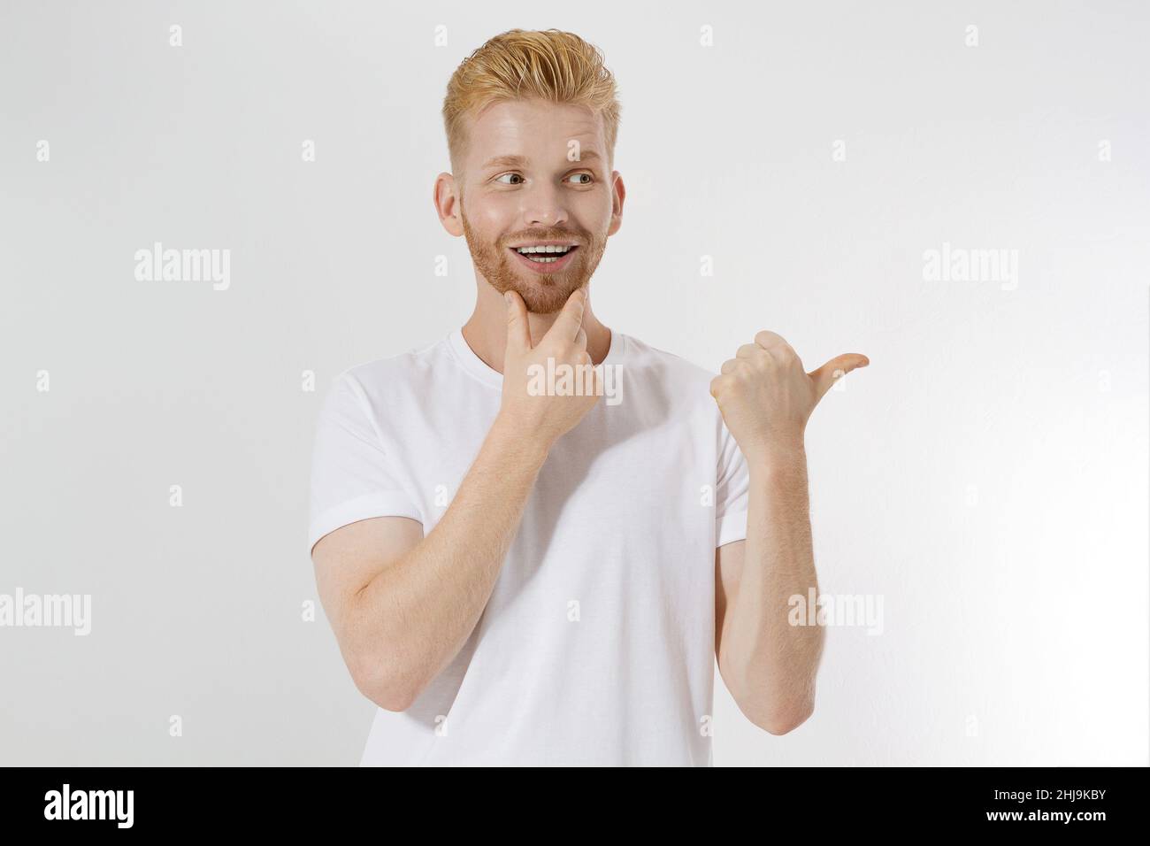 Happy young redhead guy, red stylish beard isolated. Man pointing copy space for advertising. Male in white t shirt, trend haircut. Successful young e Stock Photo