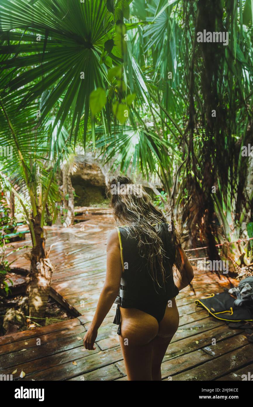 Girl walking down a wooden path in a Cenote, wearing a bikini and lifejacket, enjoying new experiences while traveling Stock Photo
