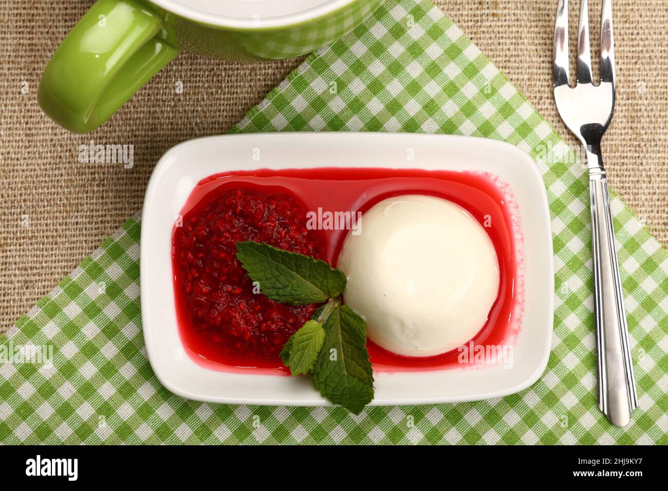 Close up serving panna cotta traditional Italian dessert with raspberry jam and cup of hot drink, elevated top view, directly above Stock Photo