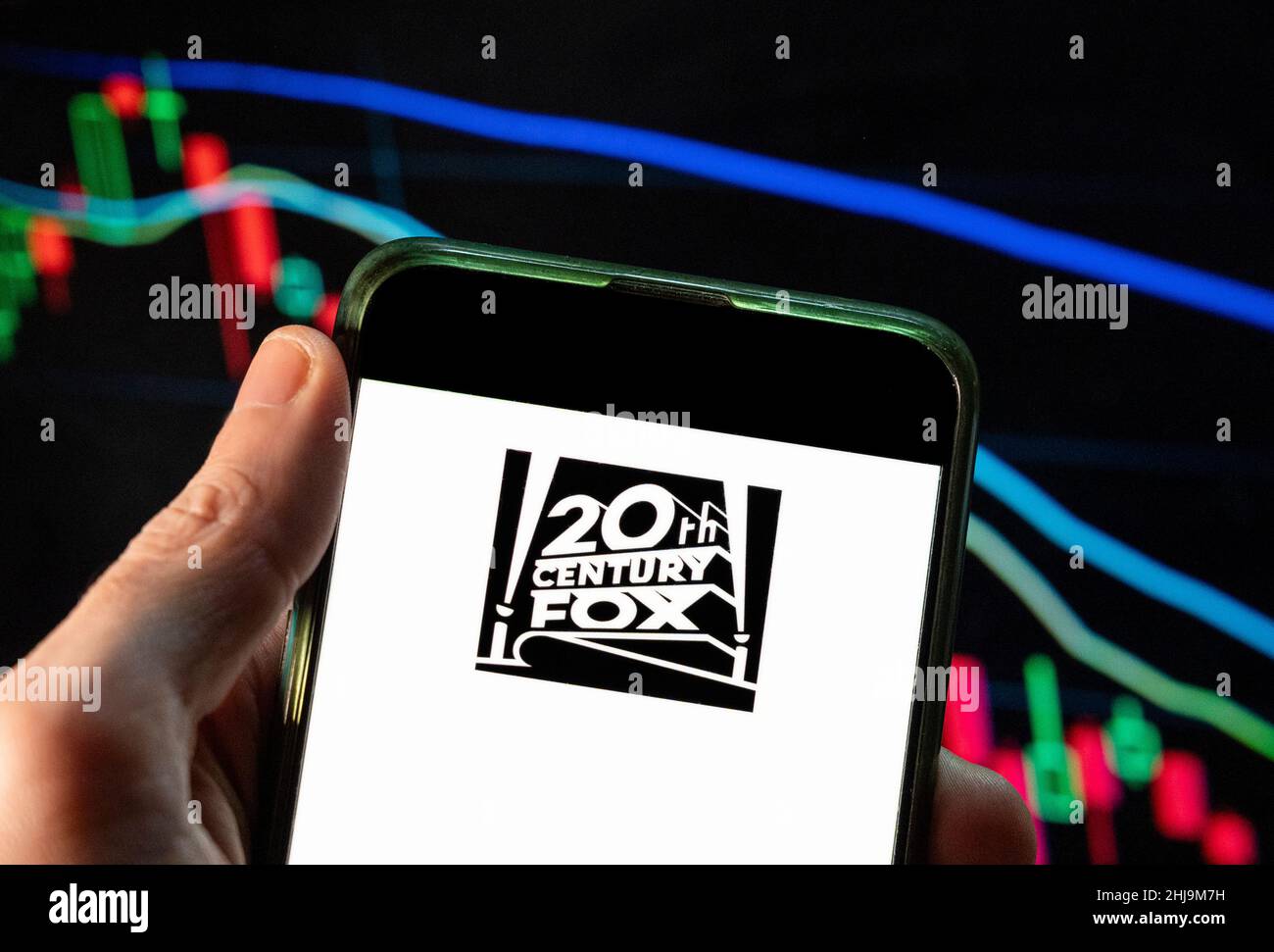 In this photo illustration the American film studio Twentieth 20th Century Fox Film Corporation logo seen displayed on a smartphone with an economic stock exchange index graph in the background. Stock Photo