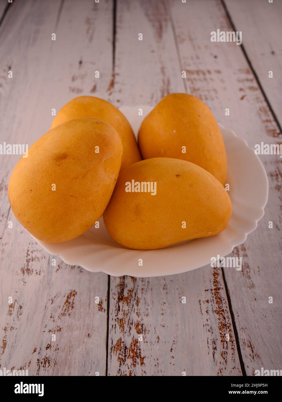 Photo shows several tropical fruits - a yellow mango. Ceramic plate with four exotic fruits is located on wooden table. The background is perfect for Stock Photo