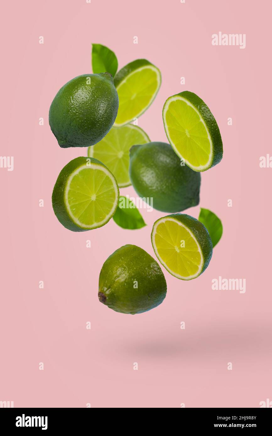 Creative idea with whole and sliced lime flying in the air isolated on pastel pink background. Minimal fruit concept. Vitamins, healthy diet concept. Stock Photo