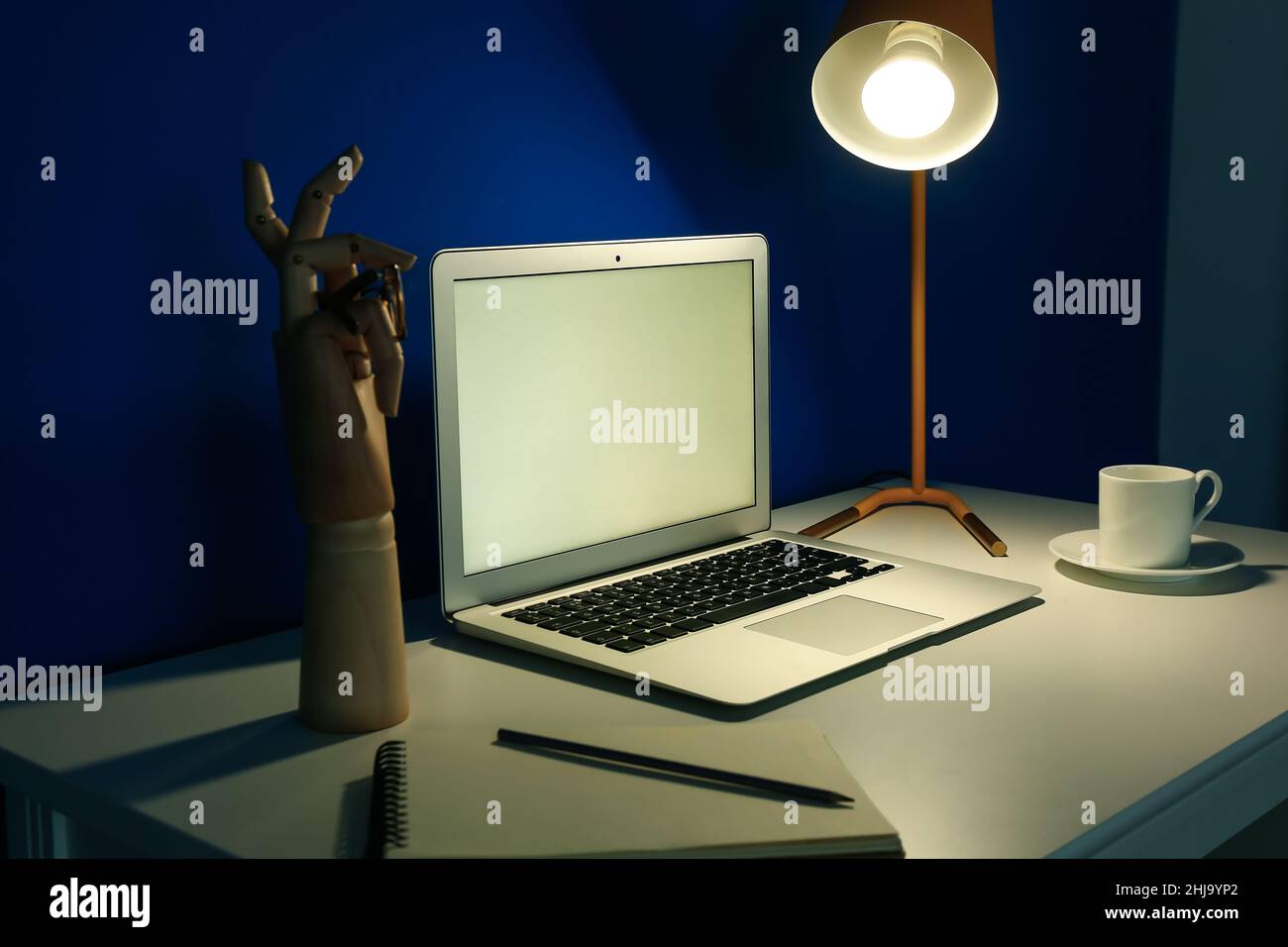 Modern workplace with open laptop and glowing lamp near blue wall in ...