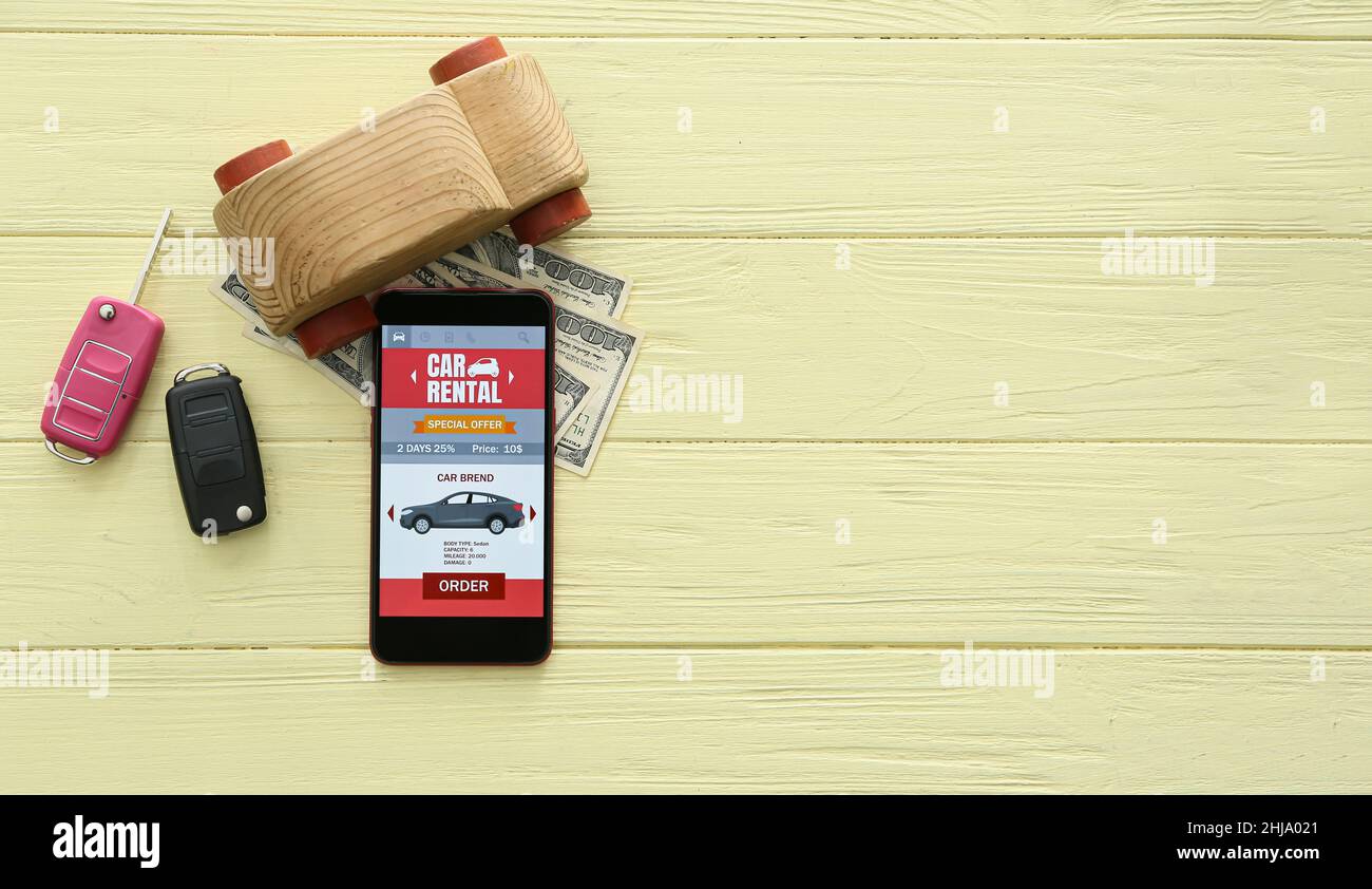 Mobile phone with open car rent app, toy, keys and money on yellow wooden background Stock Photo