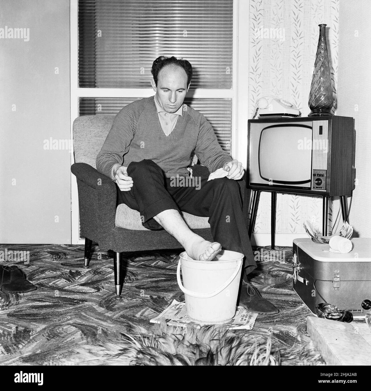 Liverpool and England international footballe Jimmy Melia soothes his injured foot in a bucket of cold water at home. 22nd April 1963. Stock Photo