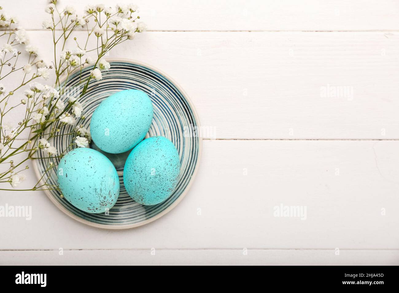 Plate with beautiful Easter eggs and gypsophila flowers on light wooden ...
