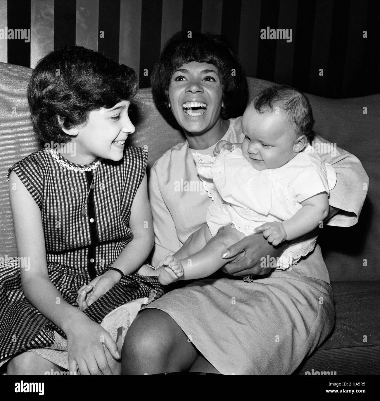 Shirley Bassey opens a new season tomorrow at the Talk of the Town. She is the first artist to be invited back to the West End night spot three times. Shirley took her two children to rehearsals, Samantha, 7 months, daughter of her marriage to Kenneth Hume, and 9-year-old Sharon. Sharon was born when Shirley was a struggling singer in Cardiff. For years she knew her mother as only Auntie Shirley, now they all live together as one family. 30th May 1964. Stock Photo