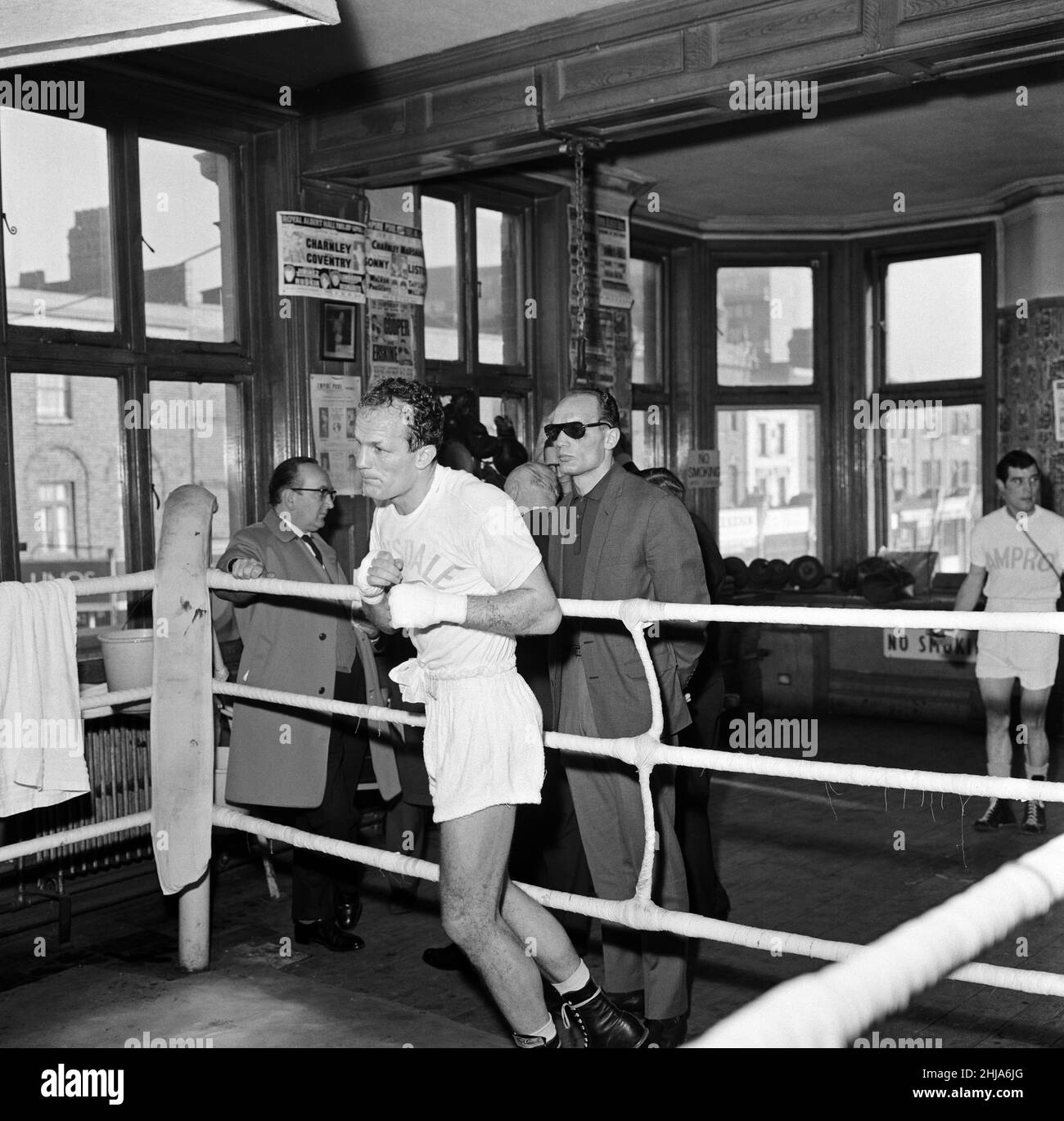 On the outside looking in, Jim Cooper (wearing sunglasses) watching his twin Henry Copper shadow box during training. Jim lost his fight against Chip Johnson and then announced his retirement from the fight game. Pictured at the Thomas A Becket, Old Kent Road, London. 12th November 1964. Stock Photo
