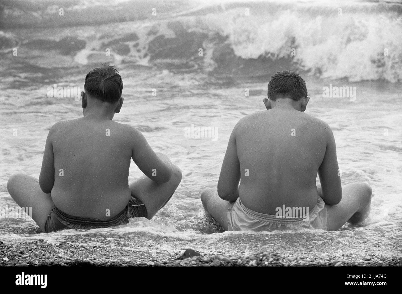 Holiday scenes at Brighton To young boys sitting in the sea to cool off during the hot weather. 7th July 1963 Stock Photo