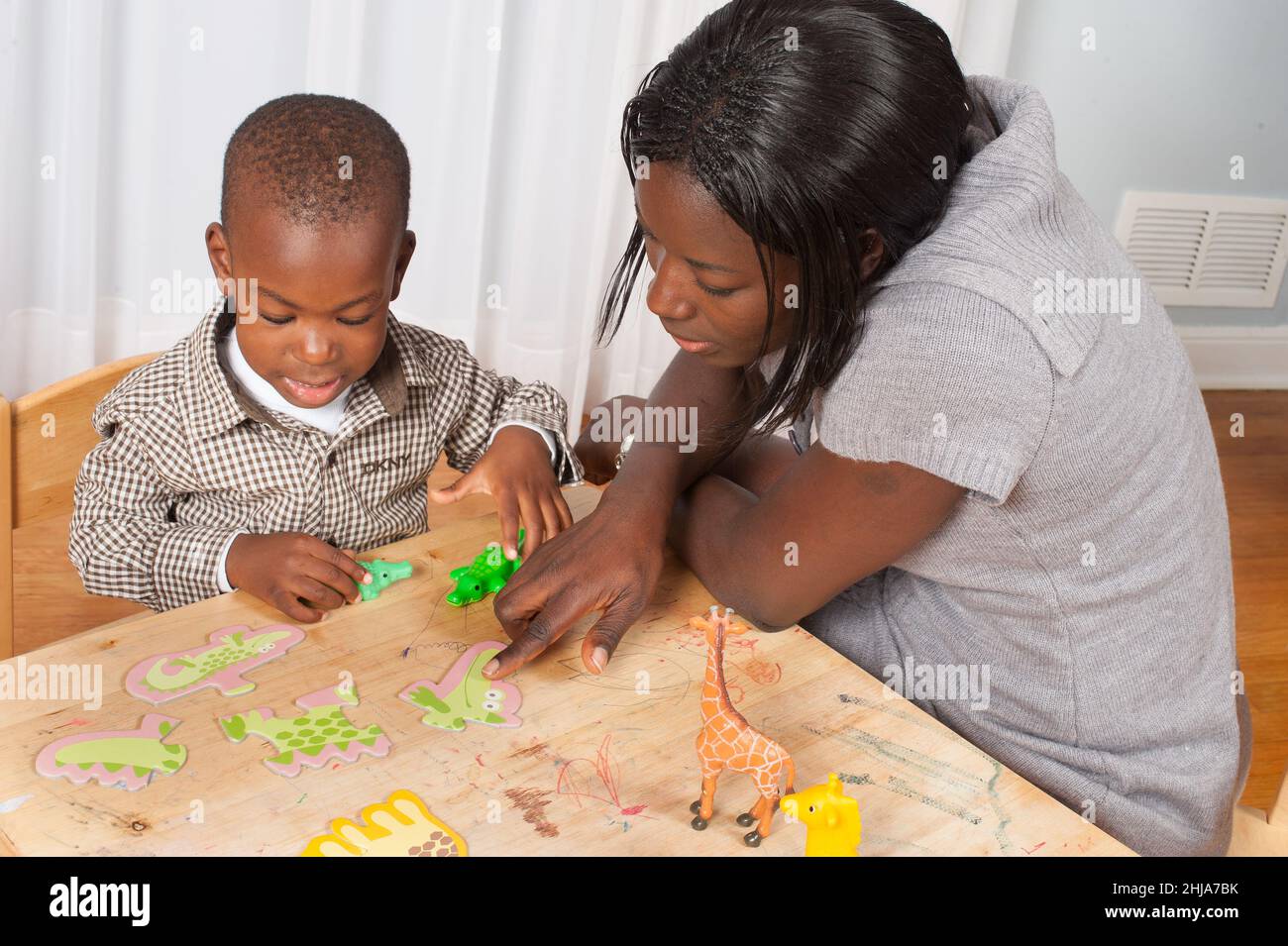 2 year old toddler boy sitting at small table playing with puzzle and toy animals, mother pointing and child naming animal Stock Photo