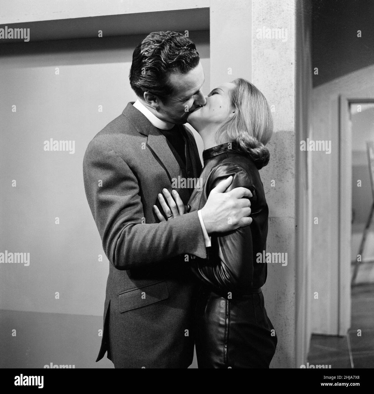 Yes, its happened in The Avengers at last, after 33 episodes and two seasons, Cathy Gale gets a lingering kiss from John Steed, It will be on the screen next Saturday (Jan. 11th). In this episode, Patrick Macnee (as John Steed) is dressed as Clergyman and of course, Honor Blackman wears her leather suit. These pictures were taken at the A.B.C studios in Teddington, where The Avengers in filmed. 5th January 1964. Stock Photo