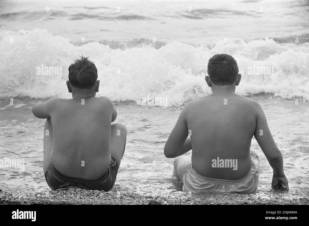 Holiday scenes at Brighton To young boys sitting in the sea to cool off during the hot weather. 7th July 1963 Stock Photo