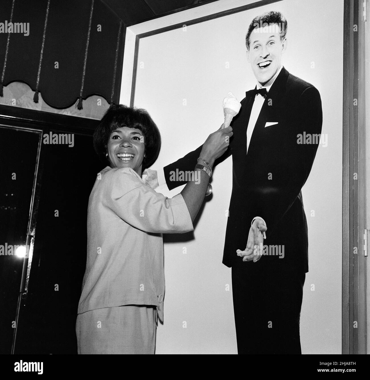 Shirley Bassey opens a new season tomorrow at the Talk of the Town. She is the first artist to be invited back to the West End night spot three times. Shirley is pictured during a break in rehearsals with a portrait of Bruce Forsyth. 30th May 1964. Stock Photo