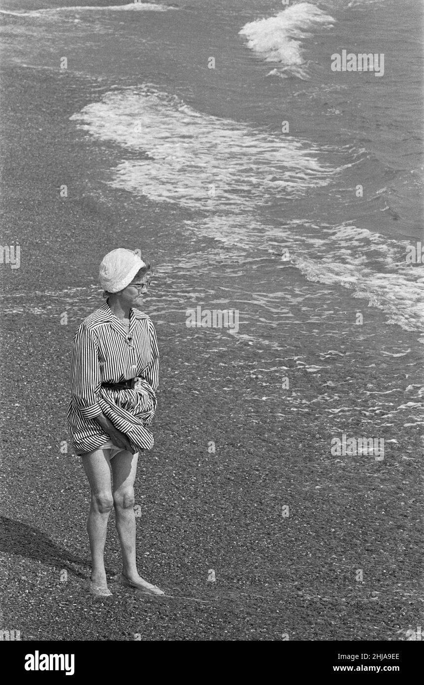 Holiday scenes at Brighton Elderly woman paddling in the sea holding her skirt up so it does get wet. 7th July 1963 Stock Photo