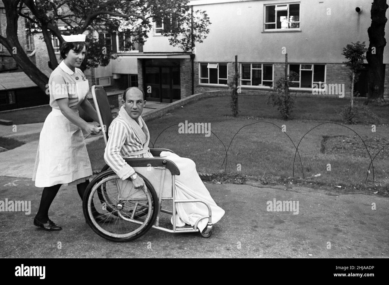 Stirling Moss, pictured in a wheelchair being pushed by a nurse, in the grounds of the Atkinson Morleys Hospital at Wimbledon. Stirling, 32, received head, arm and leg injuries in a 120 m.p.h. crash at Goodwood seven weeks ago. 11th June 1962. Stock Photo