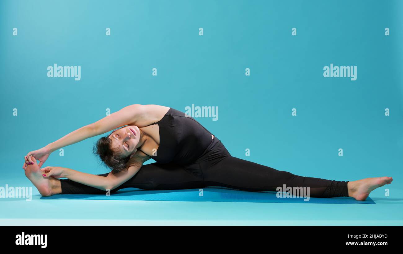 Calm adult stretching legs and arms muscles on floor mat in studio. Woman with closed eyes doing body stretch after intense workout practice, finding balance for mindfulness. Pilates training Stock Photo