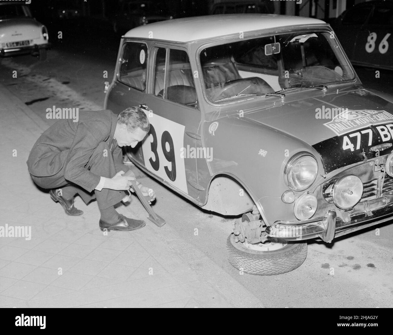 Rally driver raymond Baxter repalces the wheel of his Mini car which was removed by some other drivers as he sat in a bar at the end of the Monte carlo race.  25th January 1964. Stock Photo