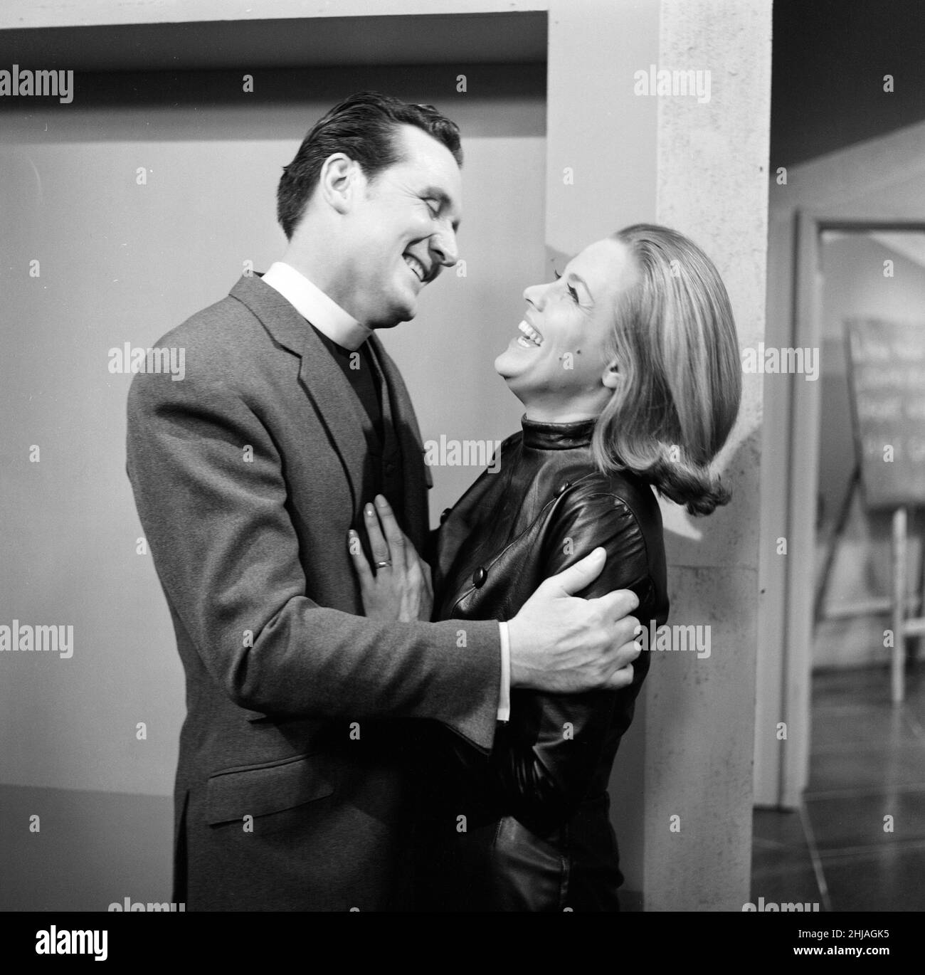 Yes, its happened in The Avengers at last, after 33 episodes and two seasons, Cathy Gale gets a lingering kiss from John Steed, It will be on the screen next Saturday (Jan. 11th). In this episode, Patrick Macnee (as John Steed) is dressed as Clergyman and of course, Honor Blackman wears her leather suit. These pictures were taken at the A.B.C studios in Teddington, where The Avengers in filmed. 5th January 1964. Stock Photo
