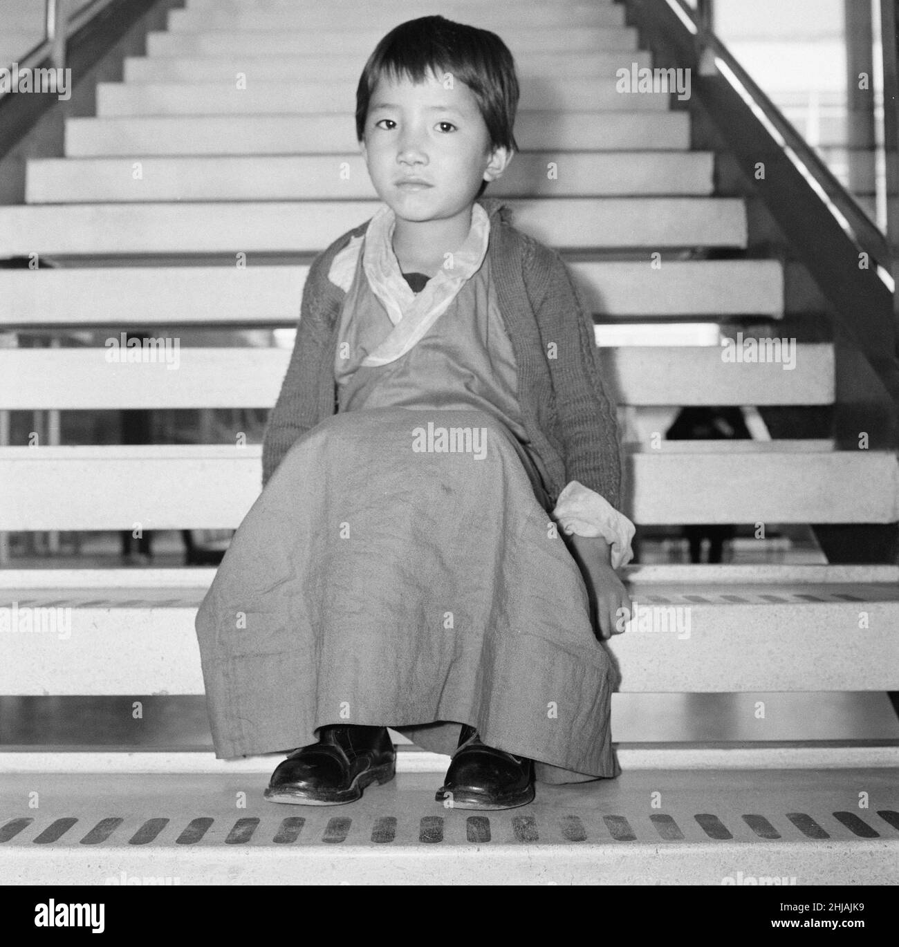 21 Tibetan Refugee Children land at London Heathrow Airport, Tuesday 26th February 1963. A BOAC Airliner brings the thirteen boys and eight girls to the UK, from a refugee camp in northern India. Many now orphaned, the children have fled chinese occupation and persecution.   Our Picture Show ... five year old Kalasang Youdon sits alone on the steps of the airport.  The children are to be relocated to the Pestalozzi Village for Children in Sedlescombe, East Sussex, which will be their new home for the next ten years.   The community is named after eighteenth century Swiss educationalist, Johann Stock Photo