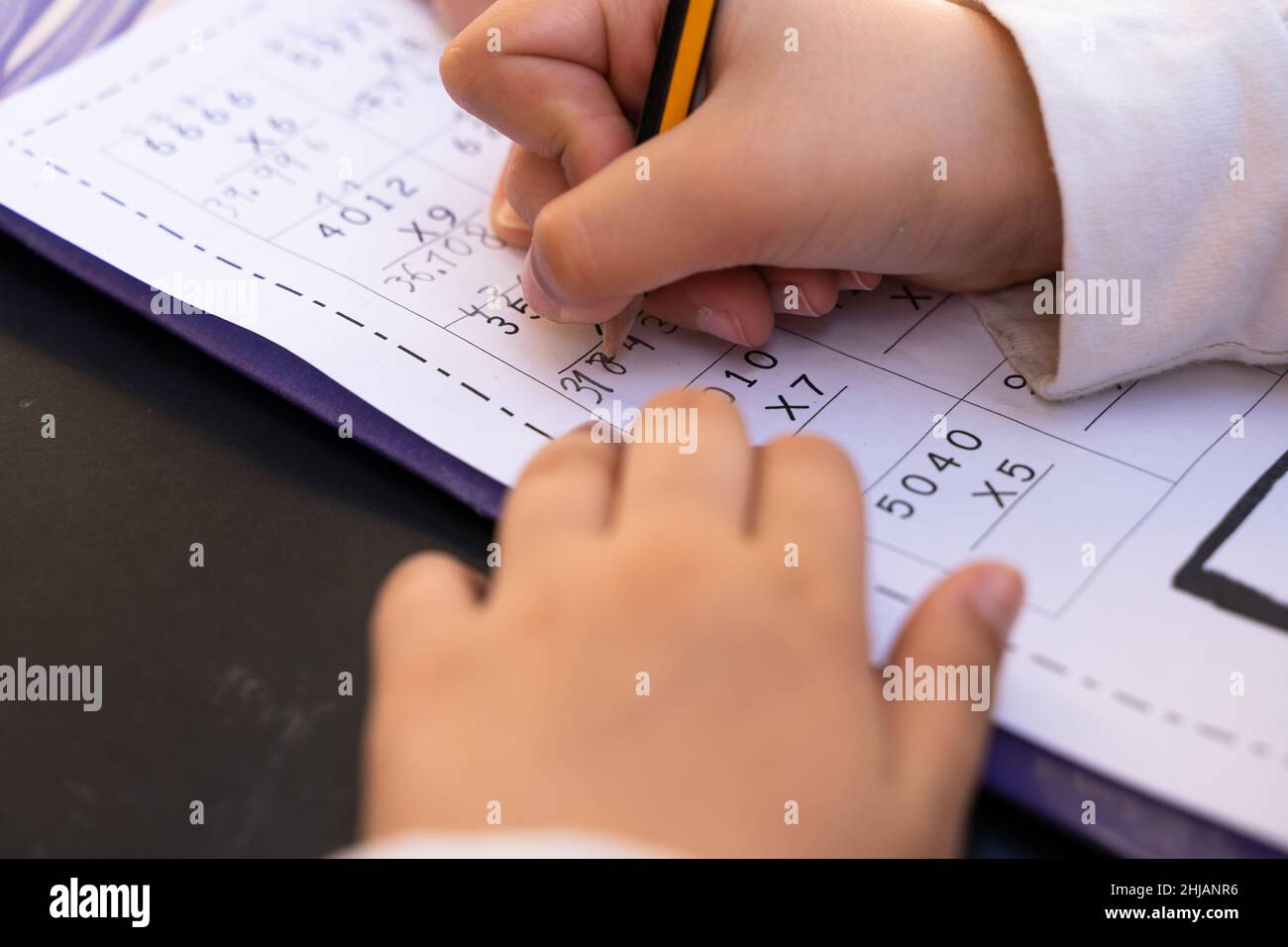 Close up on little girl hands doing school homework. Student writing with pencil maths multiplication exercise sheet Stock Photo