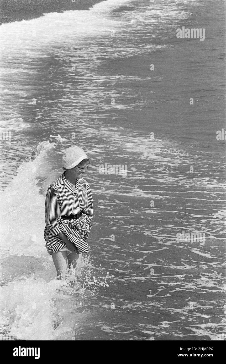 Holiday scenes at Brighton Elderly woman paddling in the sea holding her skirt up so it does get wet. 7th July 1963 Stock Photo