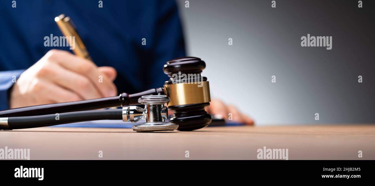 Gavel With Medical Stethoscope On Wooden Desk In Courtroom Stock Photo