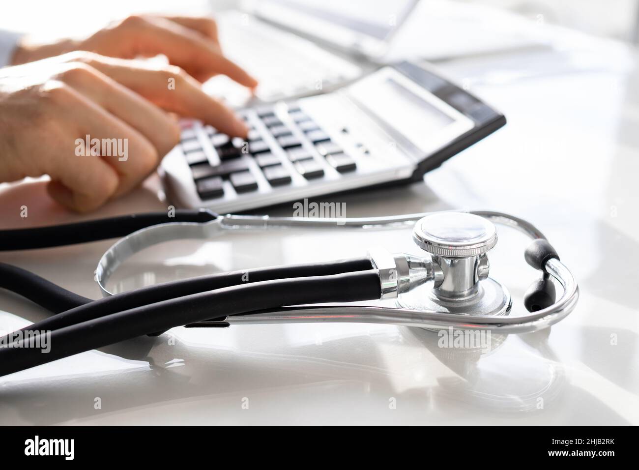 Businessman Calculating Invoice With Stethoscope On Documents At Table Stock Photo