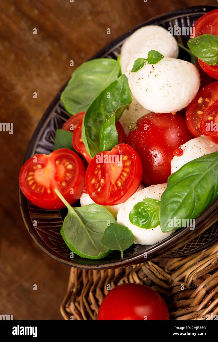 Round camembert cheese with cherry tomatoes and basil on plate. Stock Photo