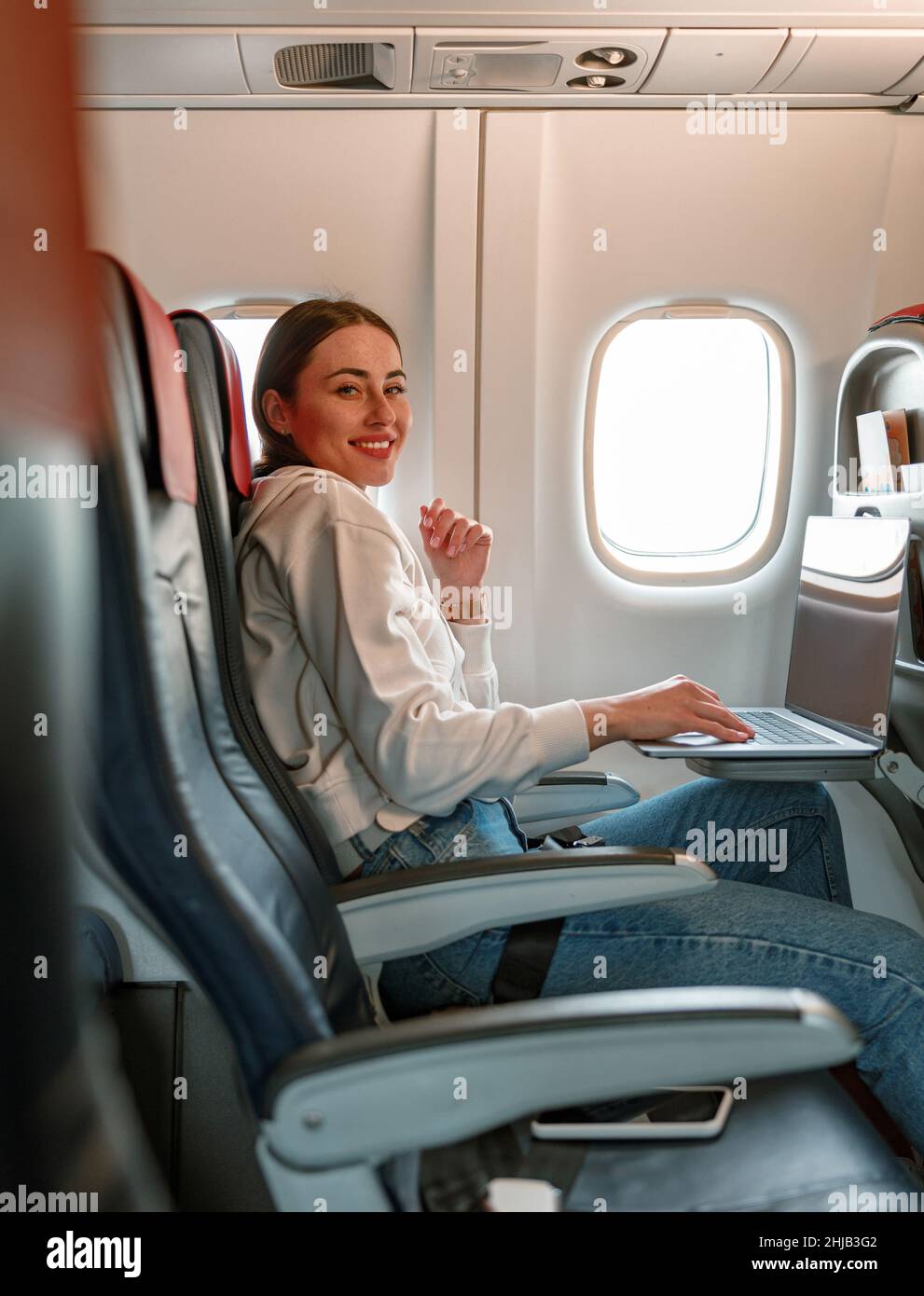 Joyful young woman using notebook in airplane Stock Photo