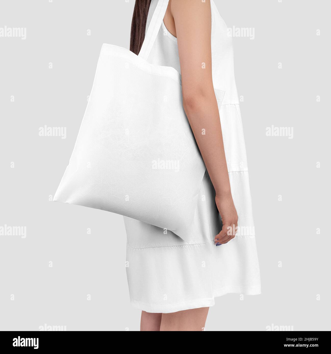 Mockup of a white totebag on a girl in a sundress, isolated on background. Template of a textured reusable bag on a model in a dress, empty sack, clot Stock Photo