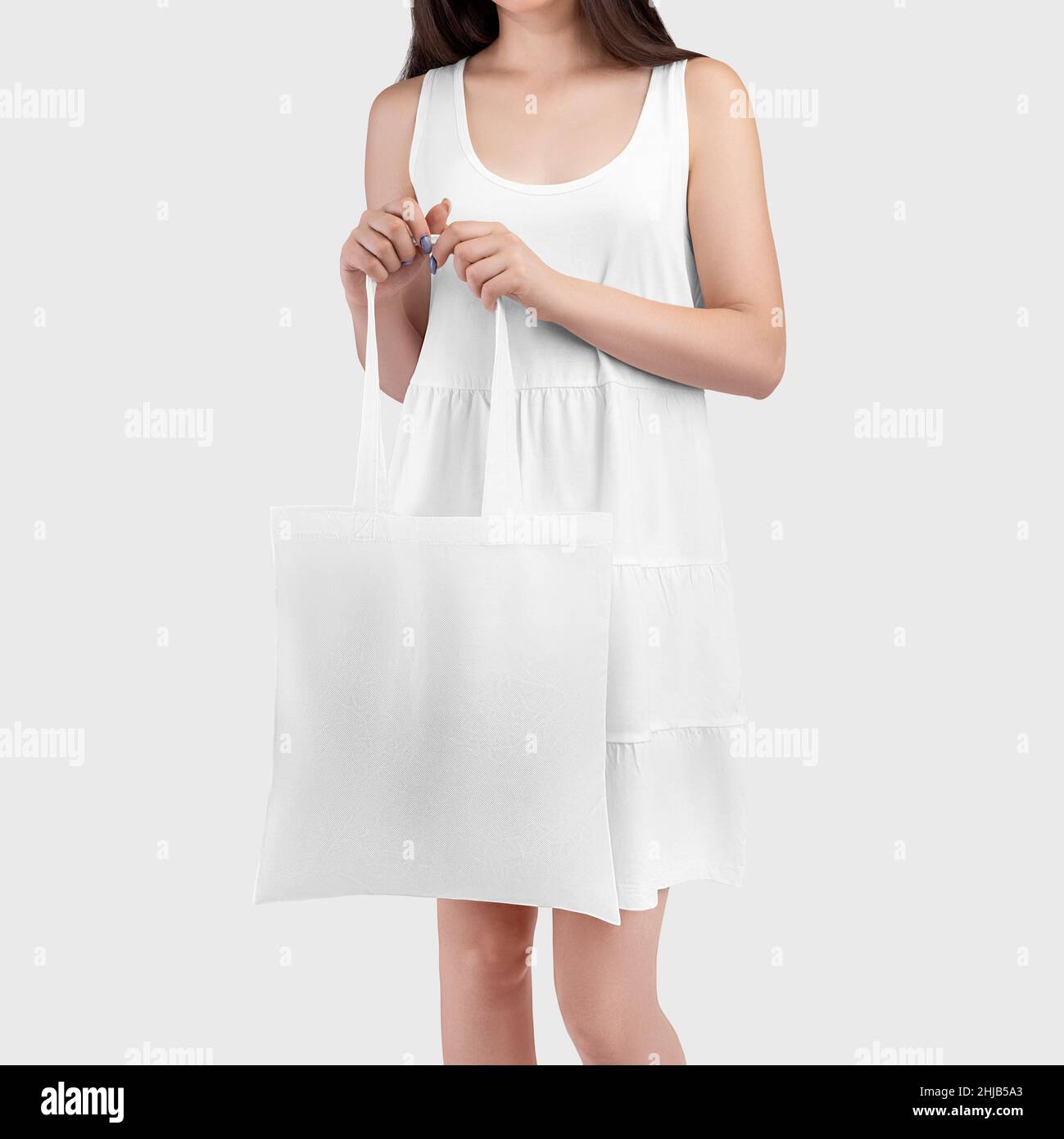 Template of a white reusable totebag in the hands of a girl in a sundress, handbag close-up, for design. Organic sack for shopping. Textured ecobag mo Stock Photo