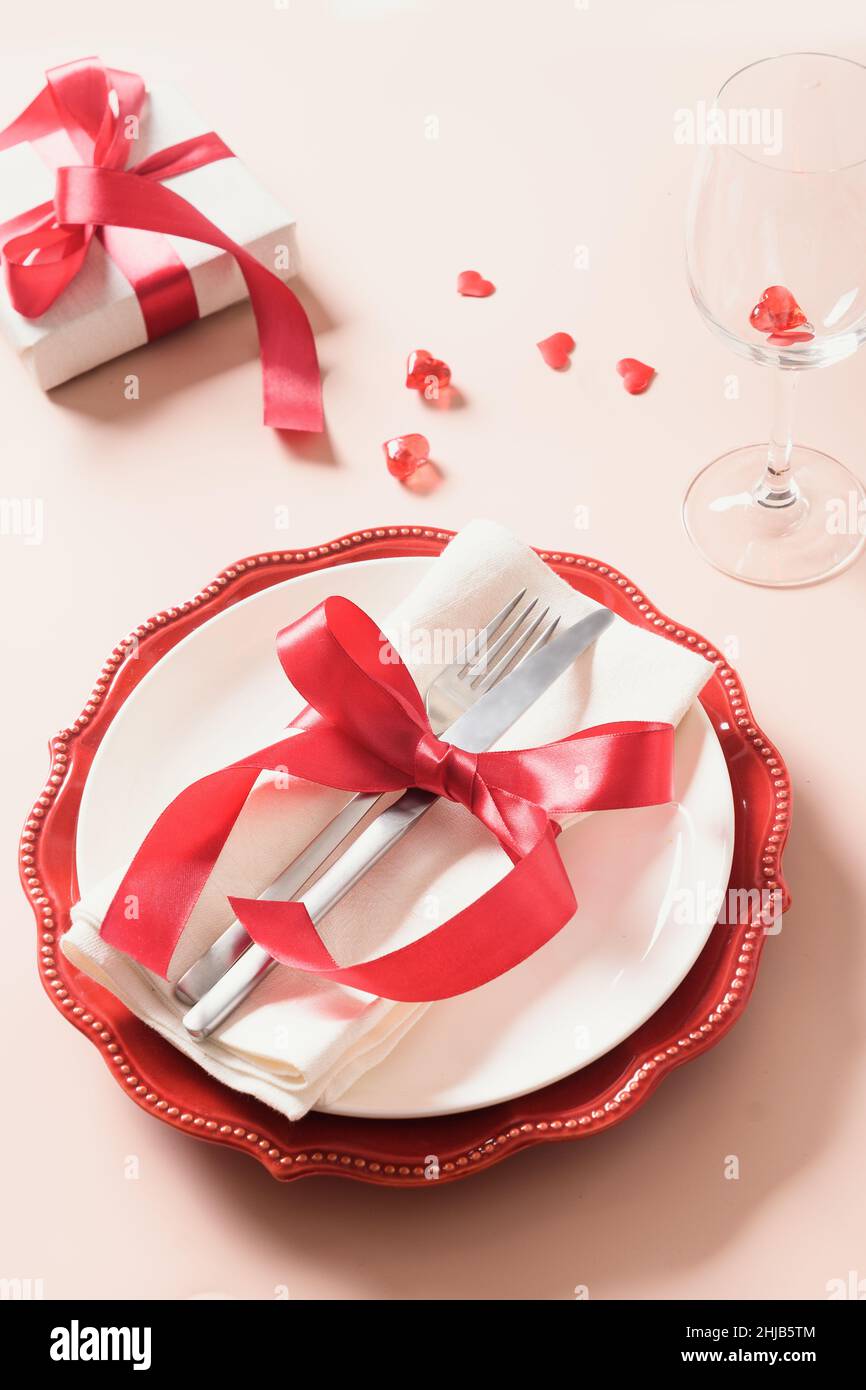 Valentines day table setting with gift, red roses, hearts on pink ...