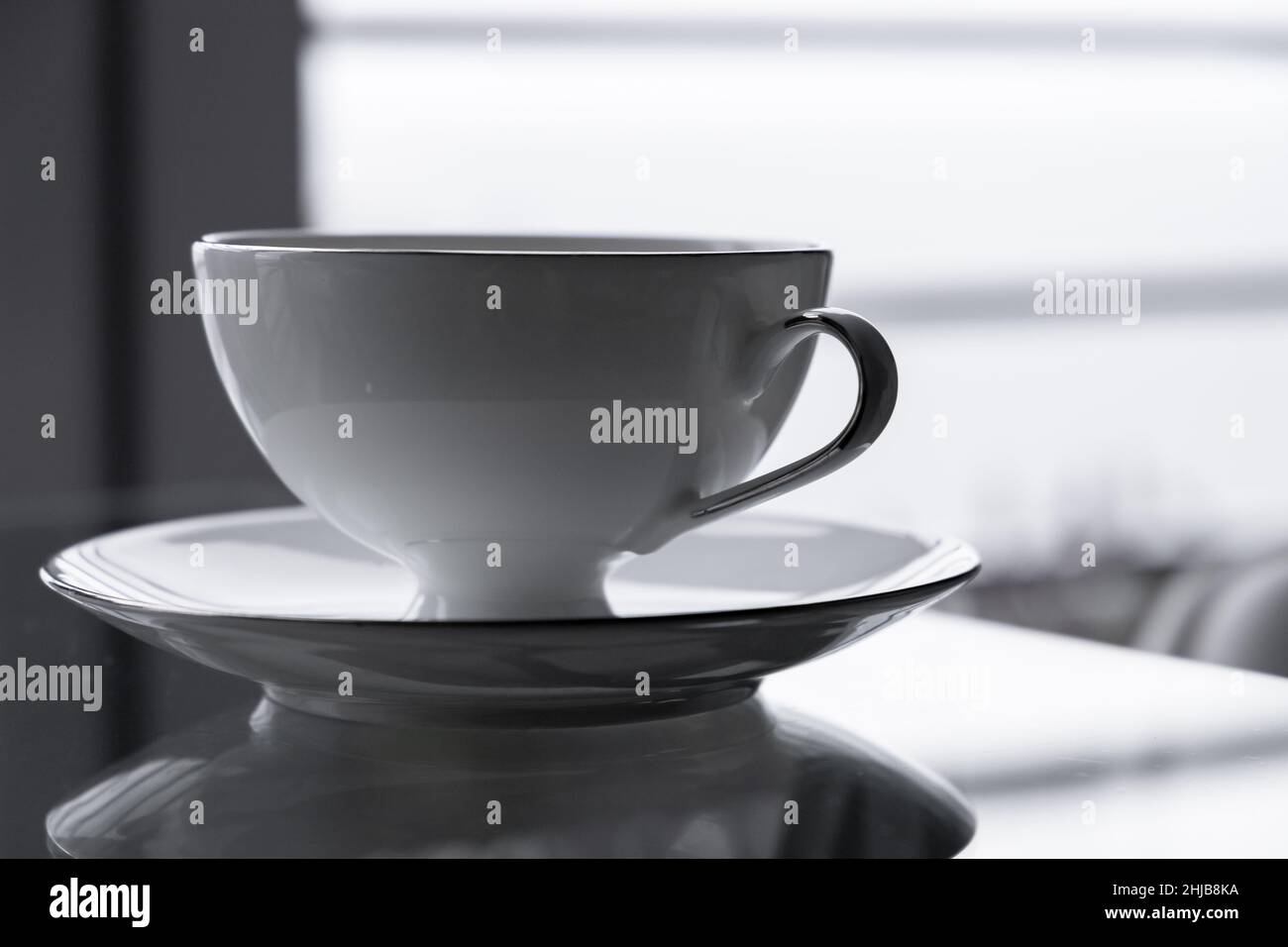 White cup and saucer stand on a glass table. Closeup photo with selective soft focus Stock Photo