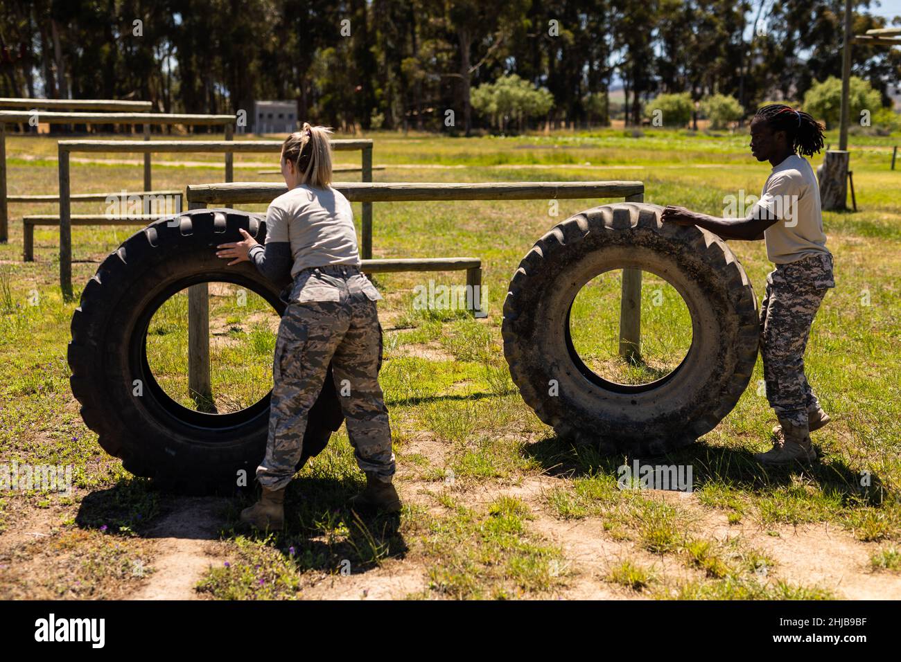 Diverse male and female soldiers rolling a tire during obstacle course at boot camp Stock Photo