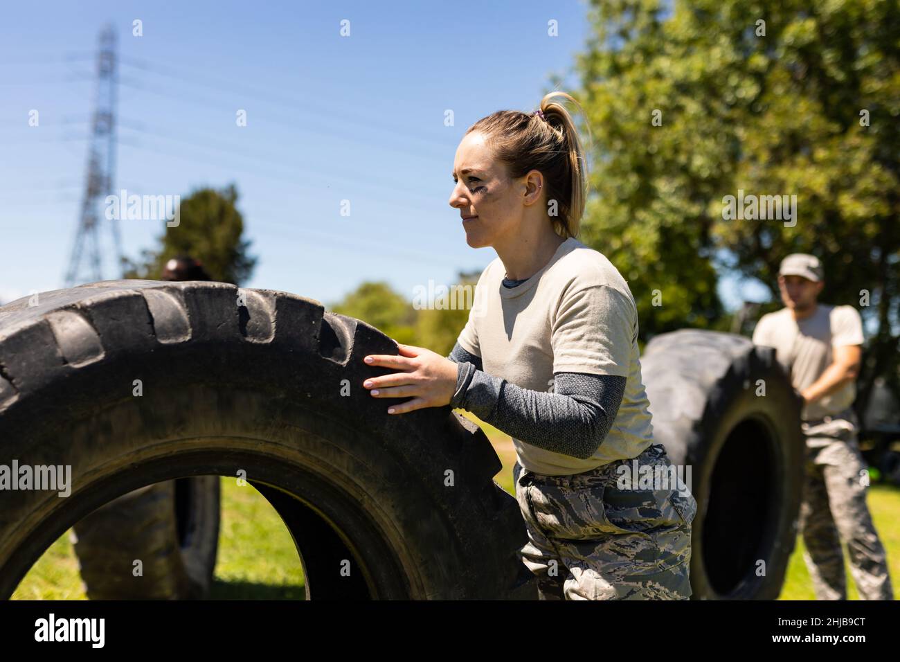 Caucasian female soldier rolling a tire during obstacle course at boot camp Stock Photo
