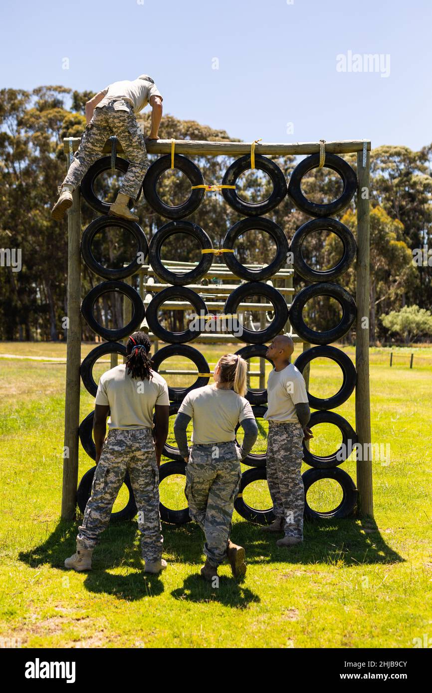 Caucasian male soldier climbing a tire wall during obstacle course at boot camp Stock Photo