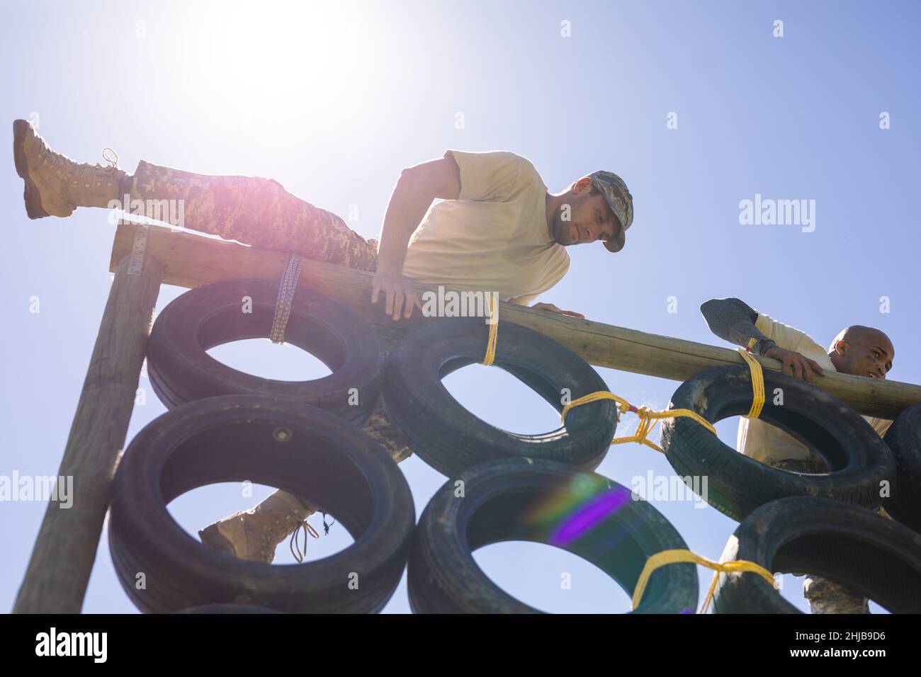 Two diverse male soldiers climbing a tire wall during obstacle course at boot camp Stock Photo